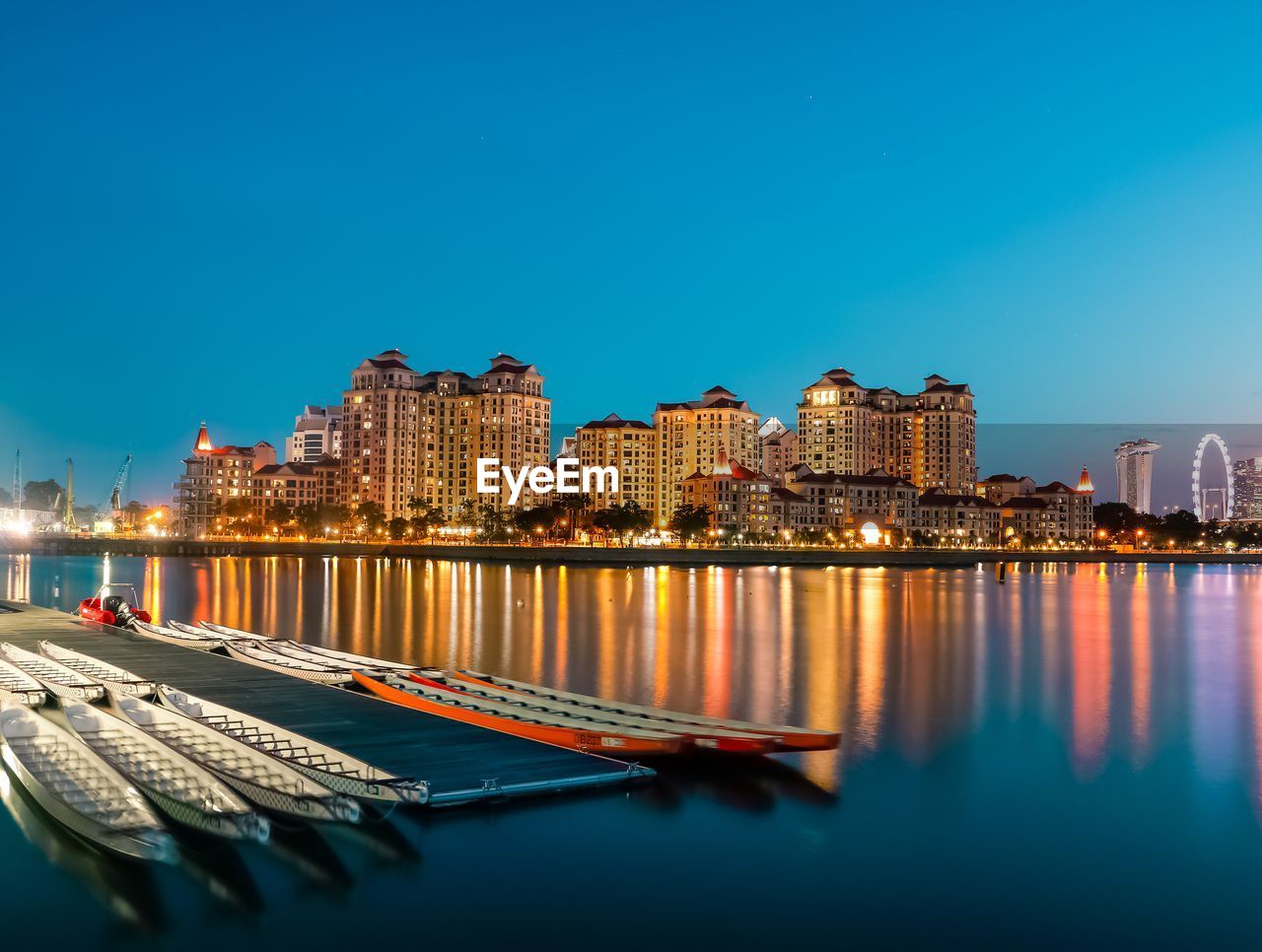 Boats moored at harbor in illuminated city against clear blue sky