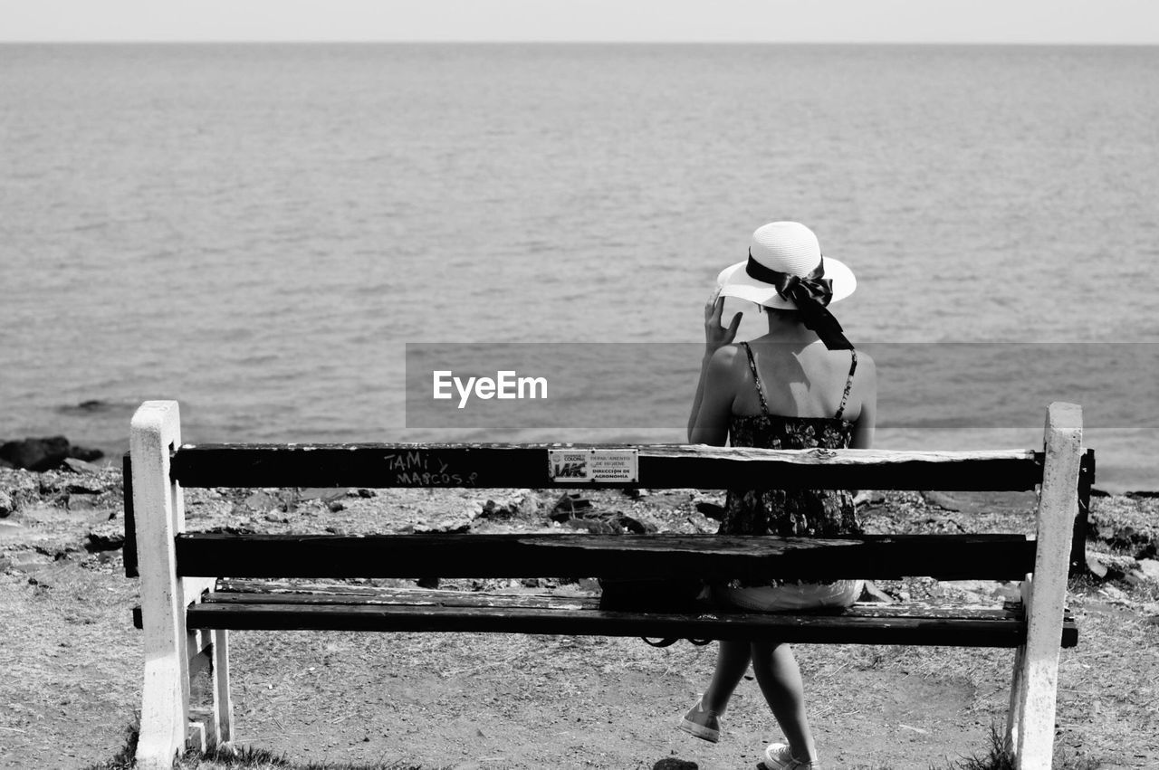 Rear view of woman sitting on bench looking at sea