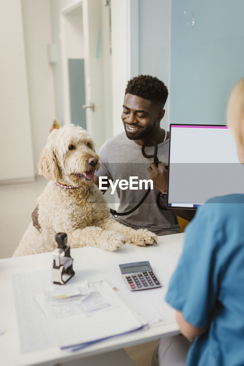 Smiling man with labradoddle looking at female vet in animal hospital