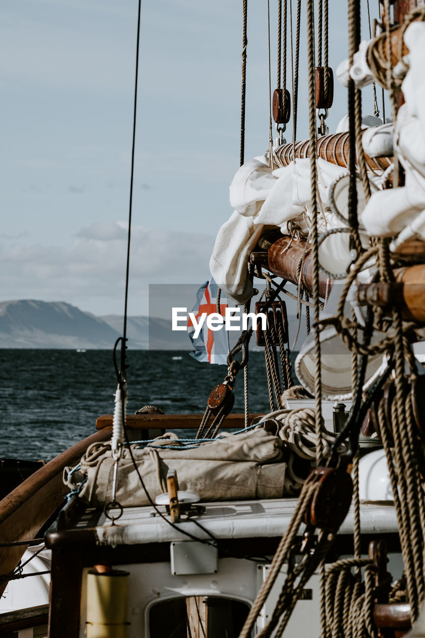 Sailing ship moving on sea by mountains against sky