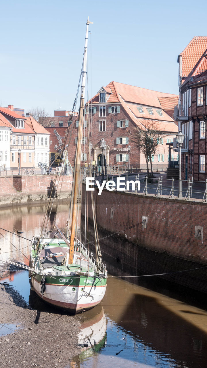 SAILBOATS MOORED IN RIVER BY BUILDINGS IN CITY