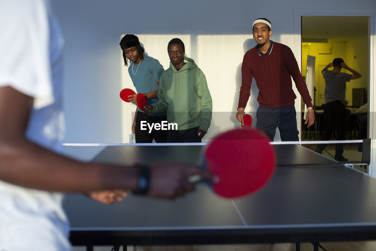 Excited friends playing table tennis in games room