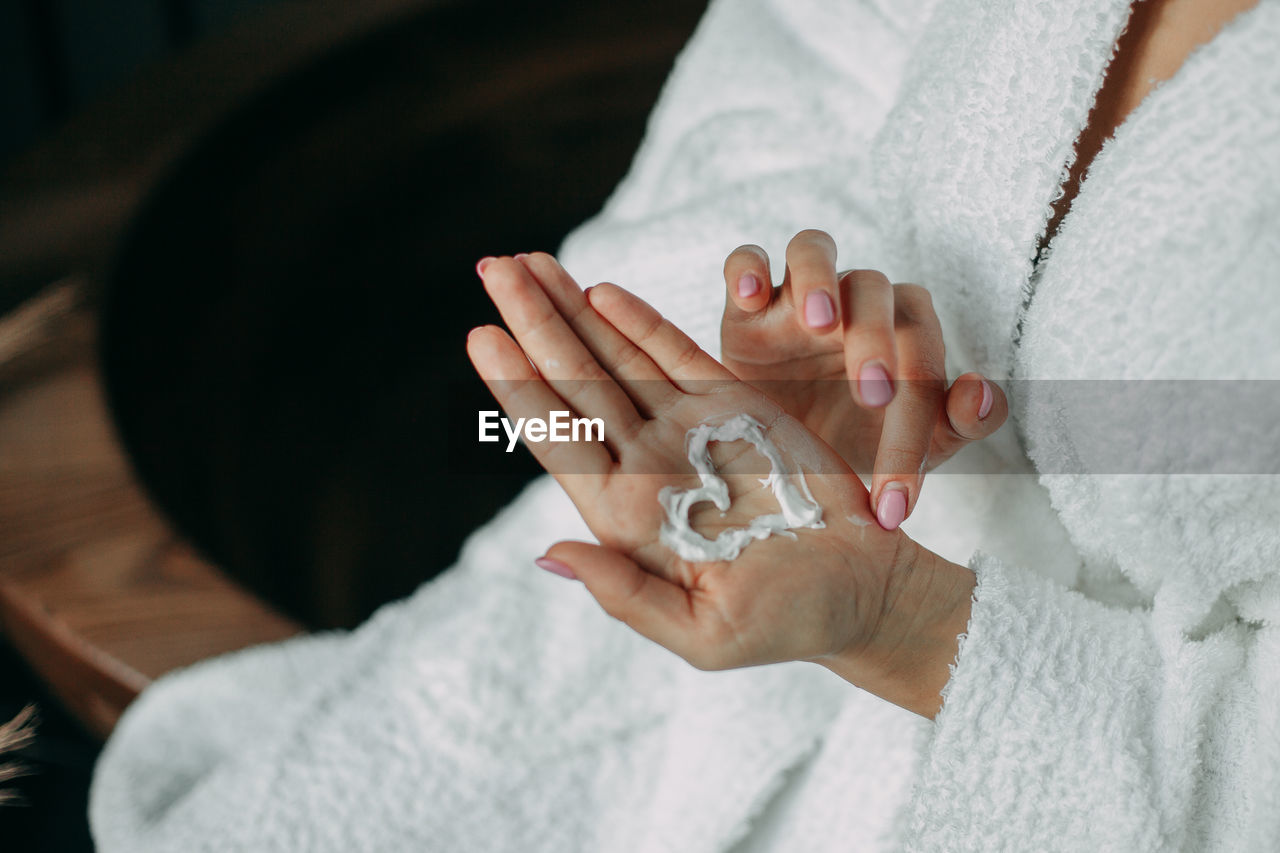 A woman in a white robe on her hand painted a heart with white cream