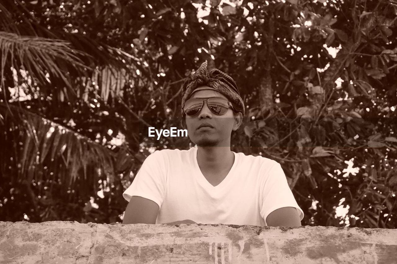 Low angle portrait of young man wearing sunglasses standing against trees