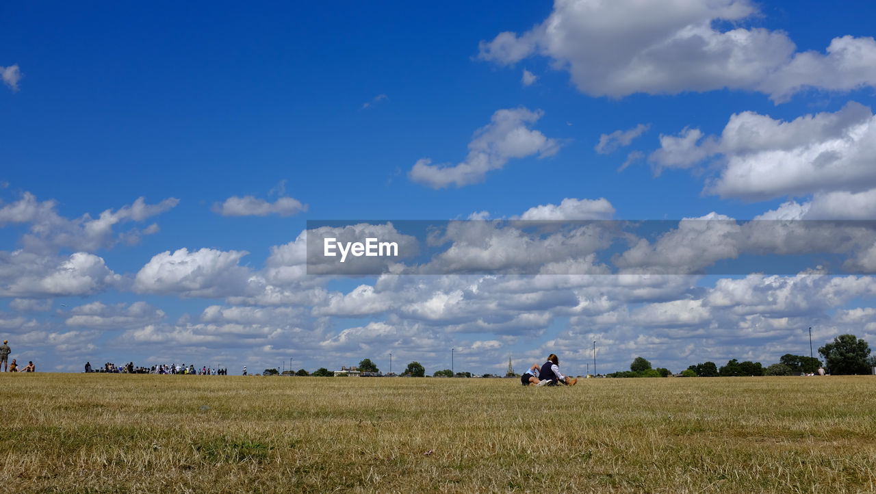 Couple sitting on field against sky