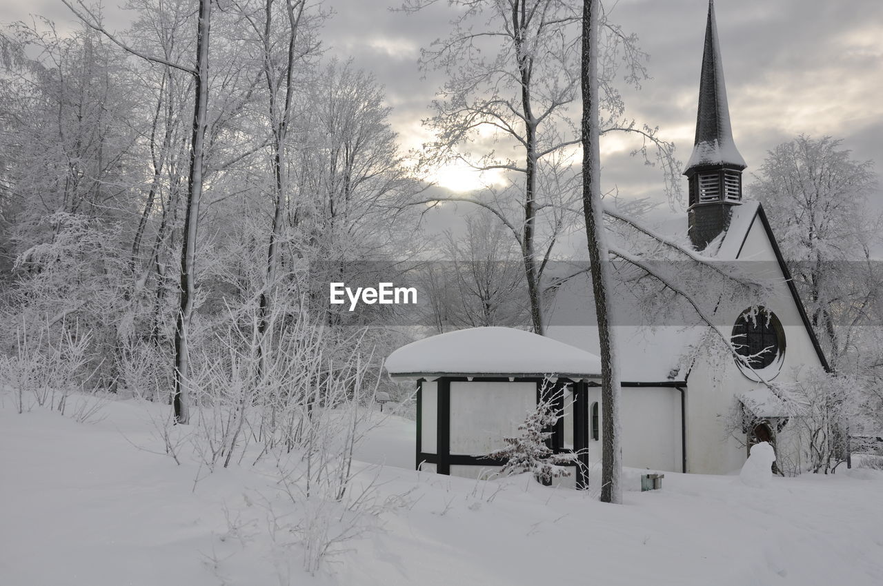 Snow covered church by trees against sky