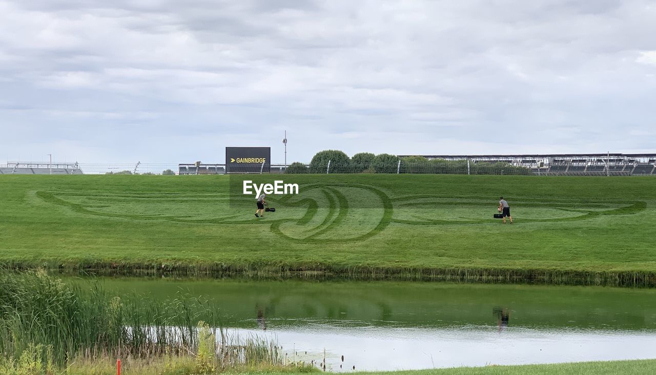 SCENIC VIEW OF GRASSY FIELD BY LAKE AGAINST SKY