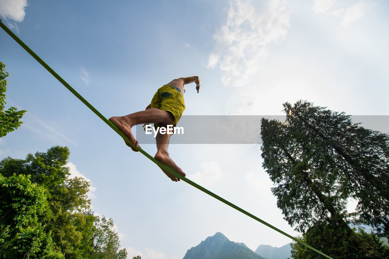 Low angle view of man walking on rope against sky