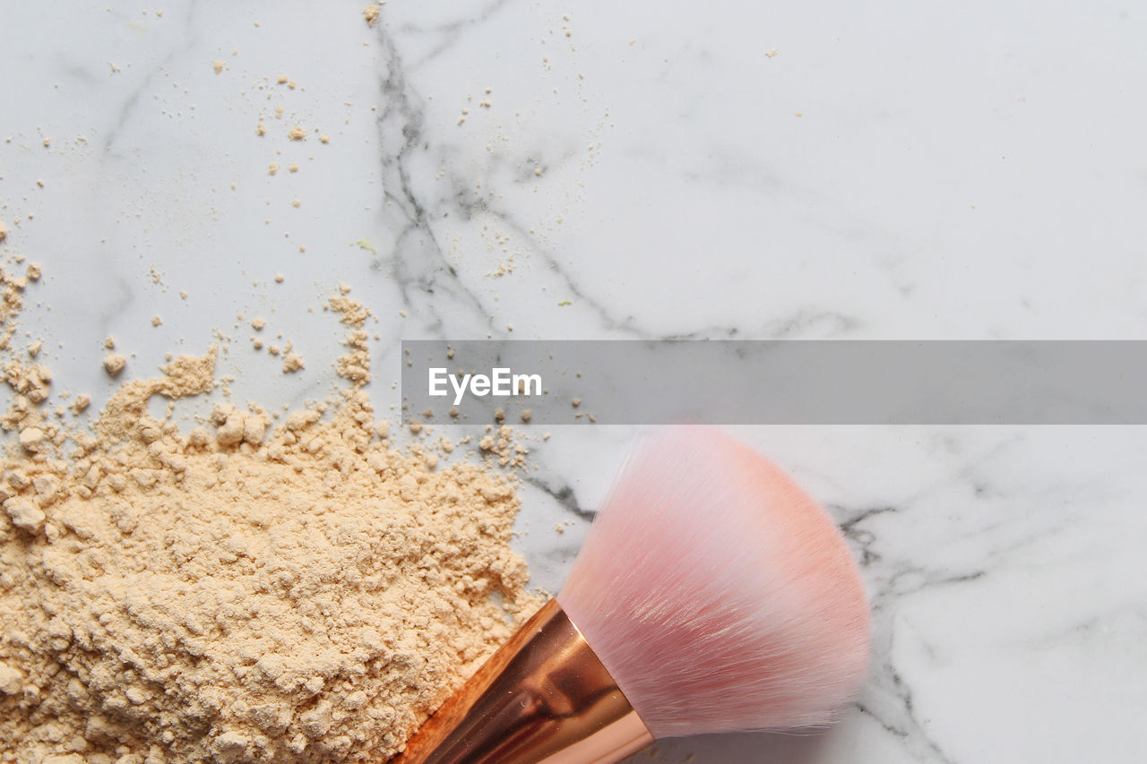 Directly above shot of make-up powder with brush over white marble