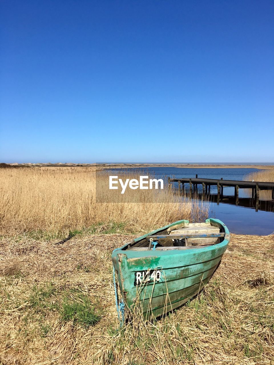 Boat moored on field against clear blue sky