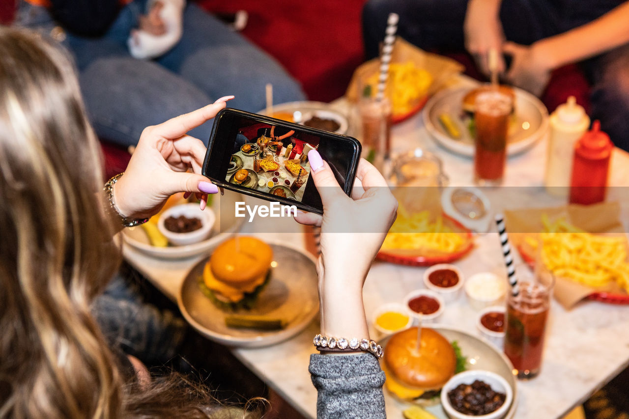 Cropped image of teenage girl photographing food and drinks served on table at restaurant