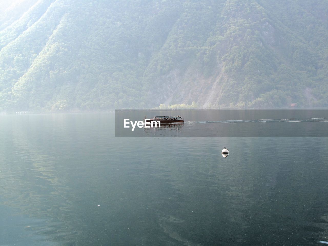 Side view of tour boat in calm lake against green mountain