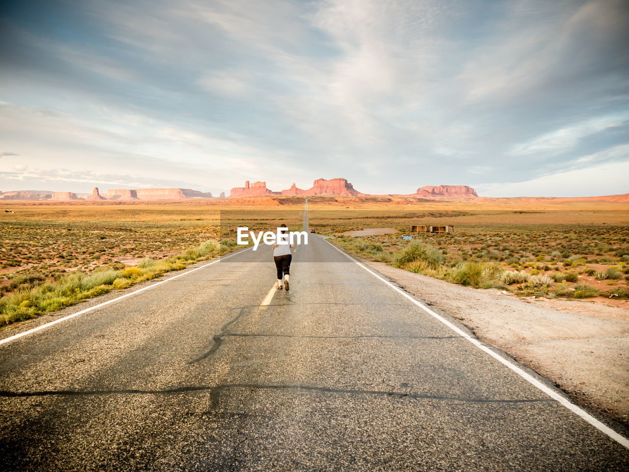 Rear view of woman running on desert road against sky