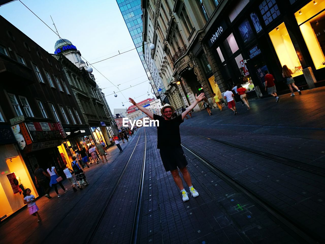 Full length of man with arms raised standing on tramway in city