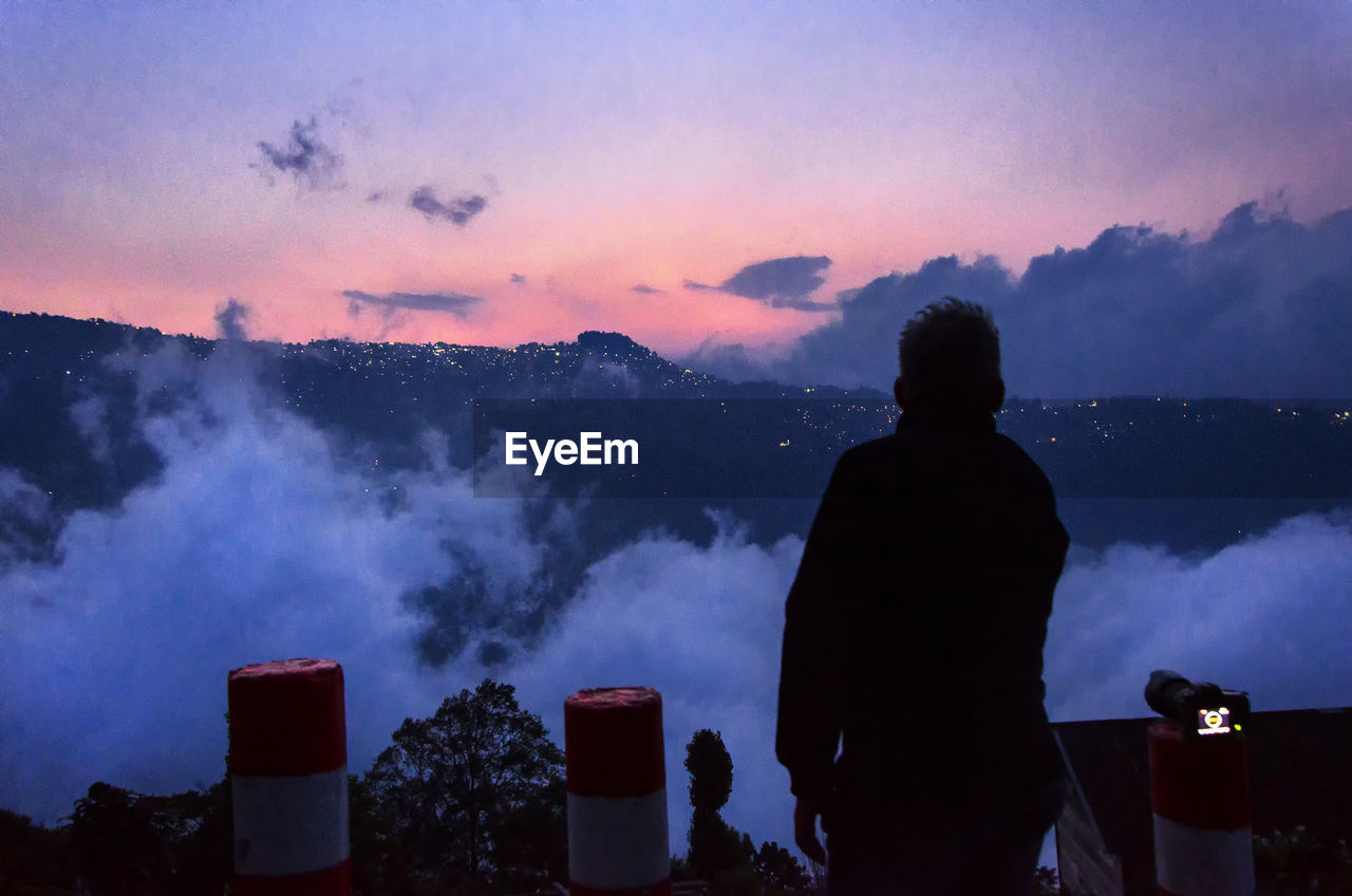 Rear view of man standing against cloudy sky during sunset