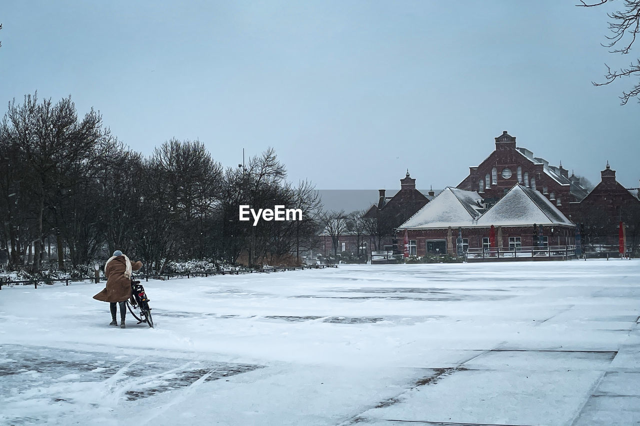 WOMAN ON SNOW FIELD BY TREES AGAINST SKY