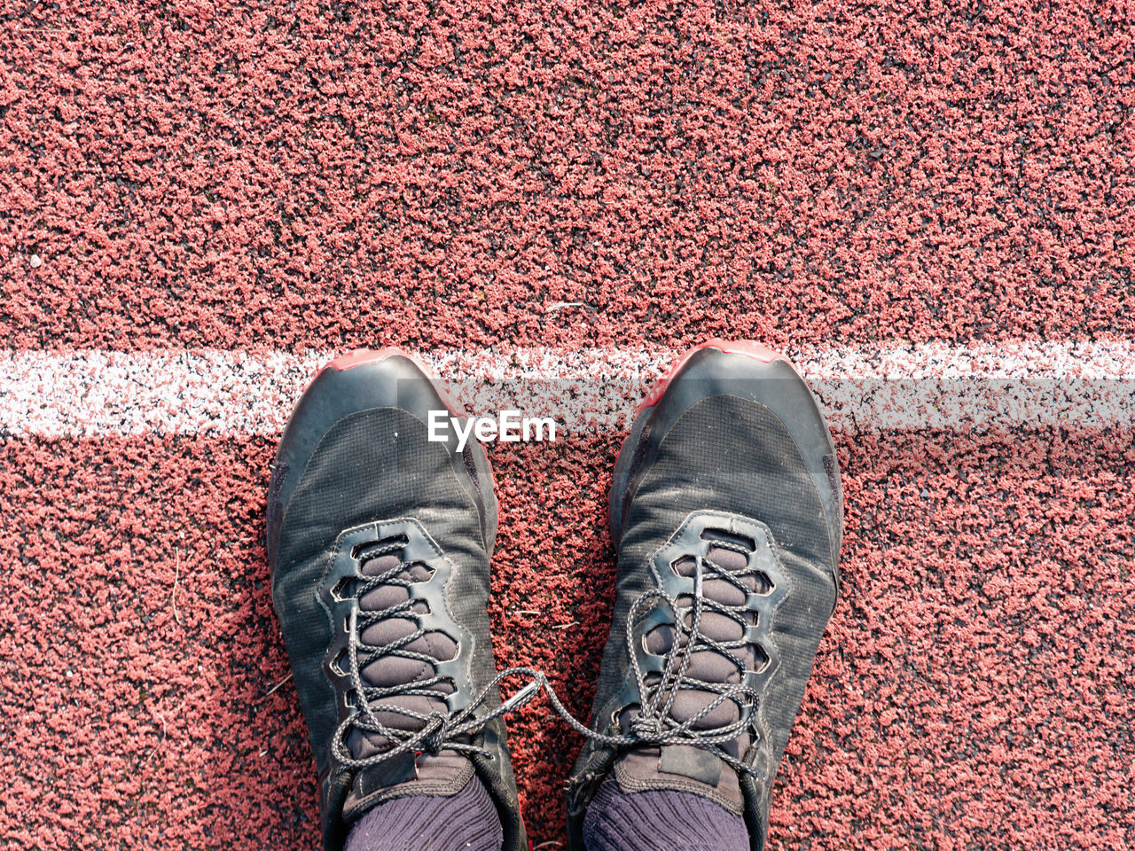 Feet in sneakers stand near the starting line on the red asphalt. bounding line