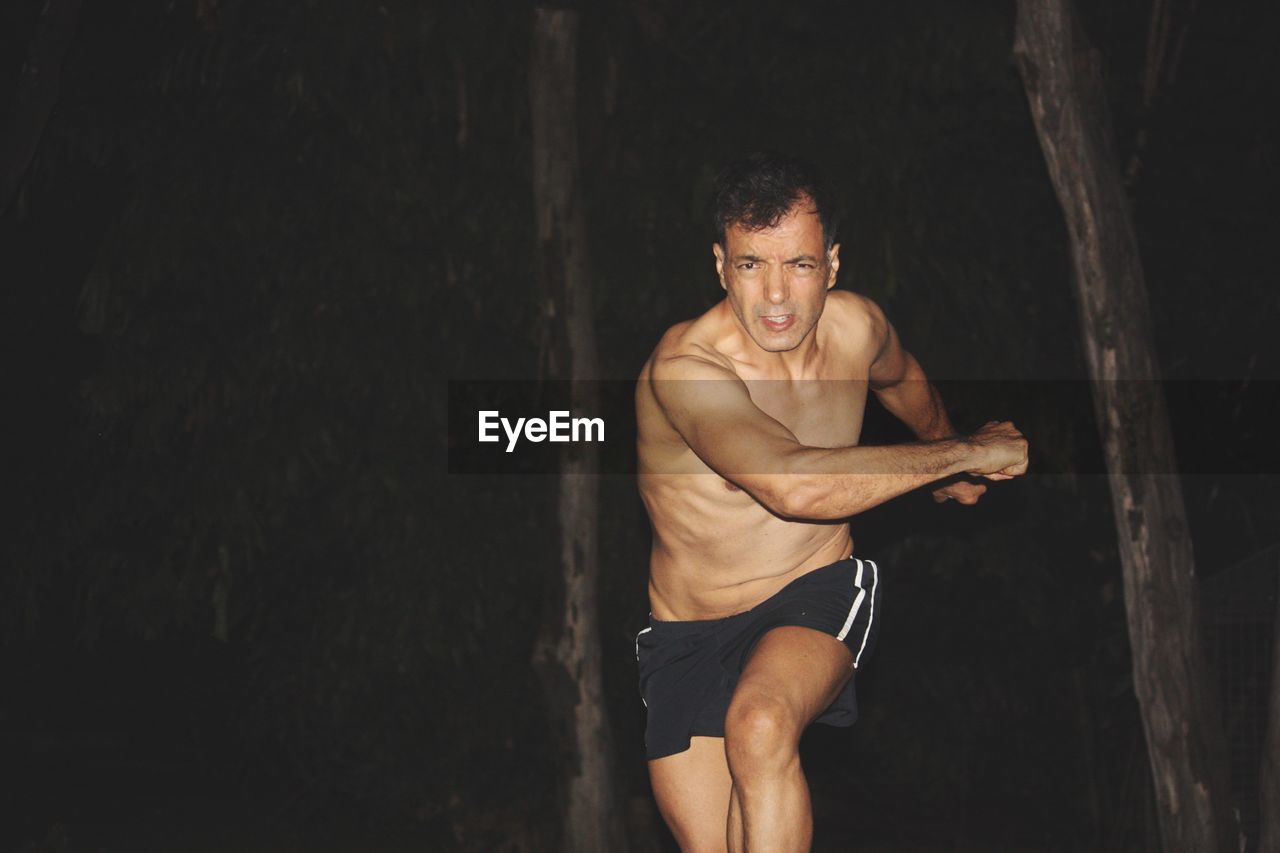 Portrait of shirtless man running against trees