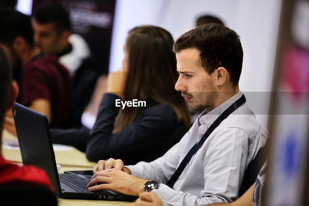 Side view of young man using laptop while sitting on chair