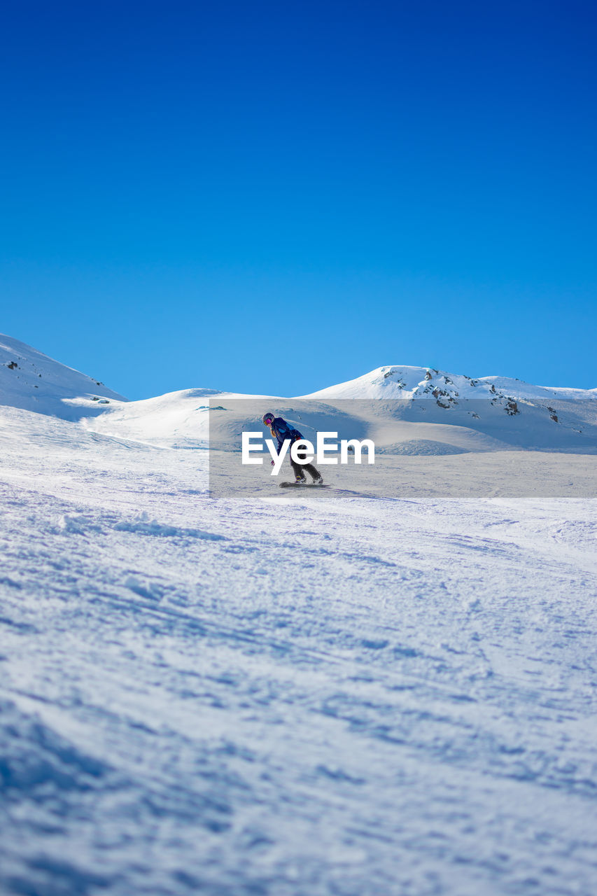 Woman skiing on snowcapped mountain against clear blue sky