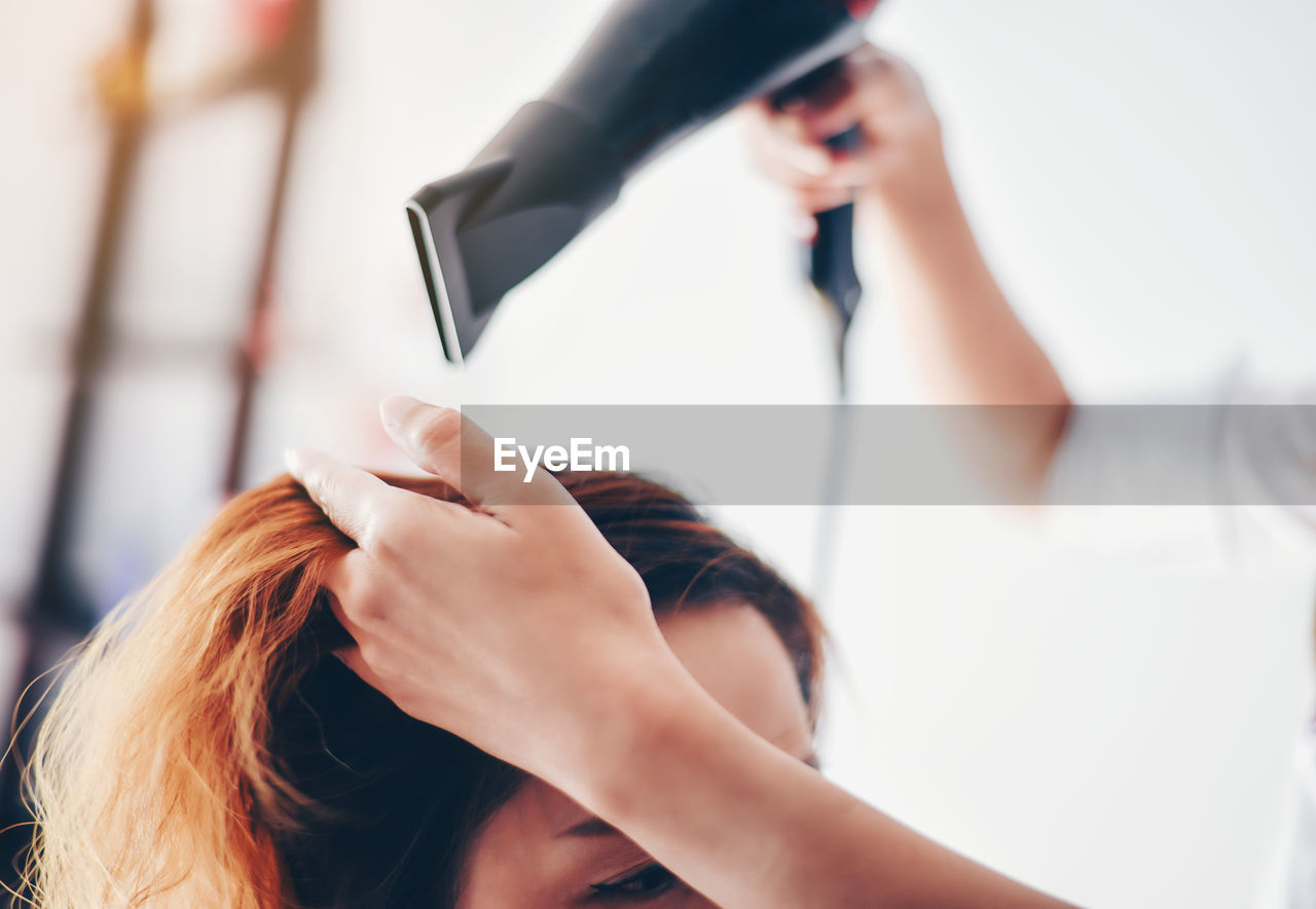 Cropped hand of beautician straightening woman hair in hair salon