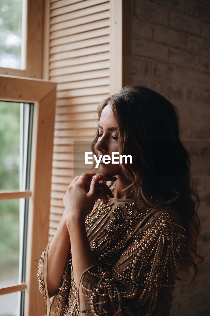 Young woman with eyes closed standing by window at home