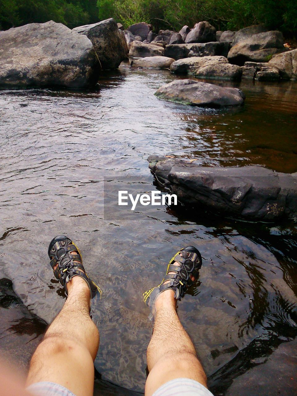 Low section of man sitting on rock at stream