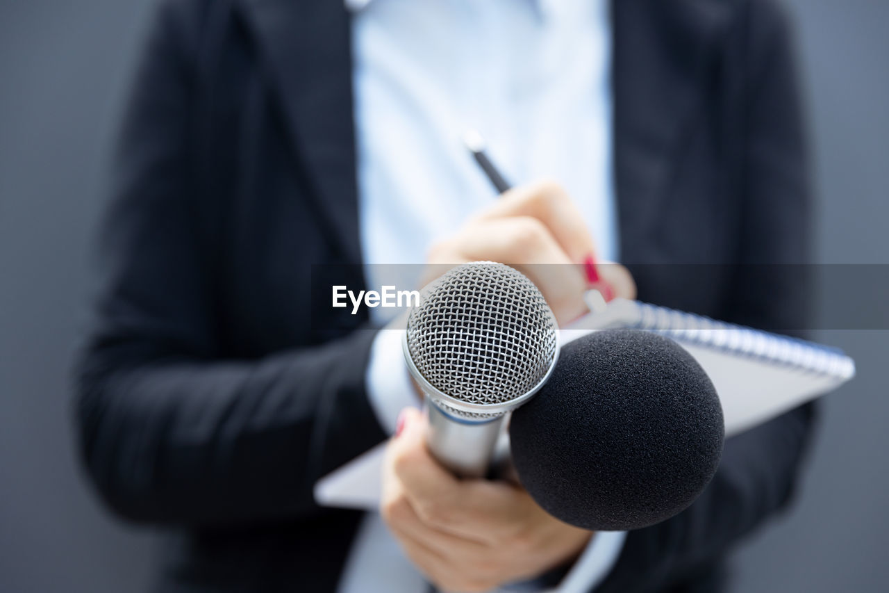 Female journalist at news conference or media event, writing notes, holding microphone