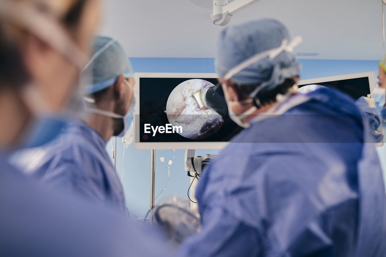 Professionals monitoring surgery on computer screen while standing in operating room