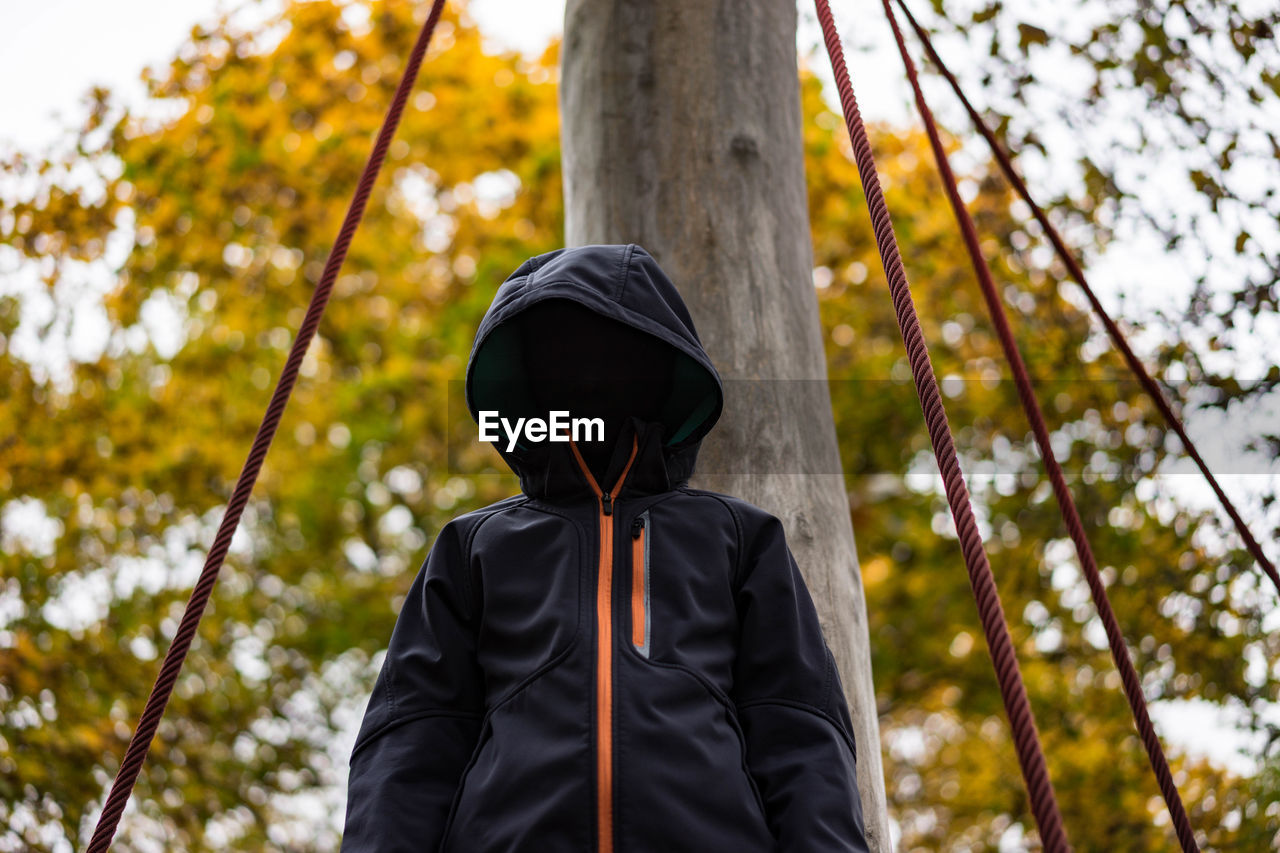 Low angle view of boy wearing hooded shirt against pole