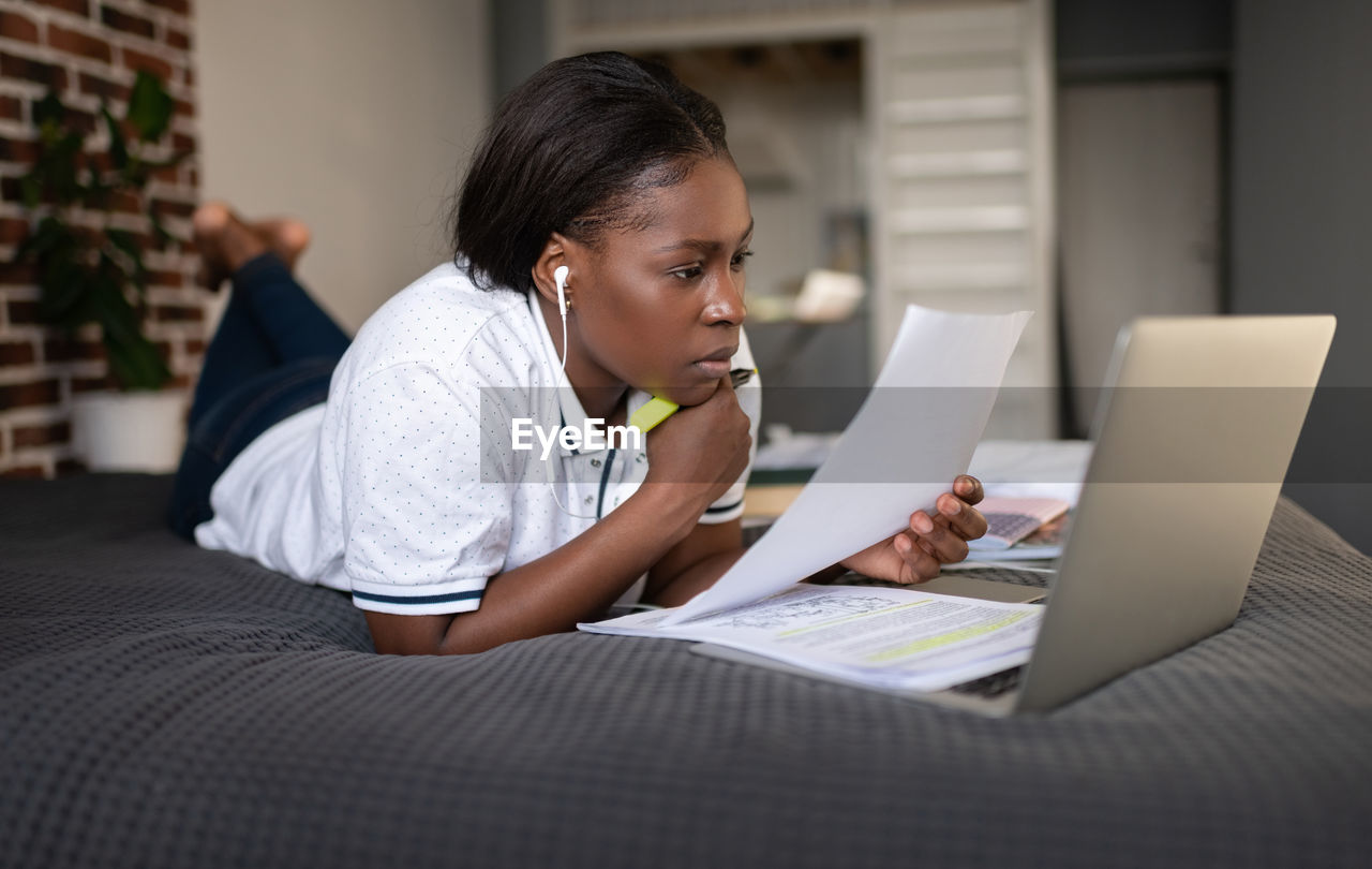 Thoughtful black woman reading paper during online lesson