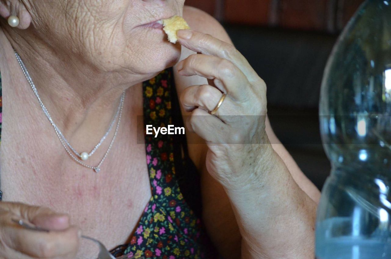 Midsection of senior woman eating plum at home