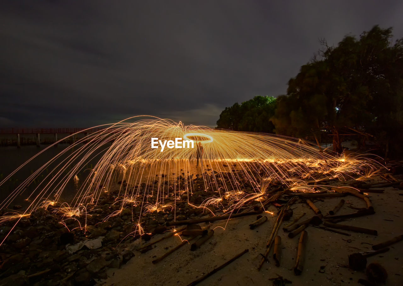 Man spinning wire wool at beach against sky at night
