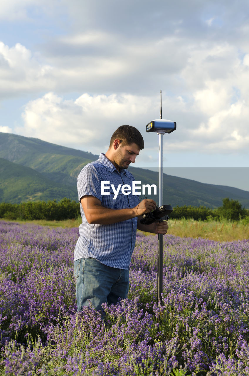Surveyor with theodolite on lavender field against sky