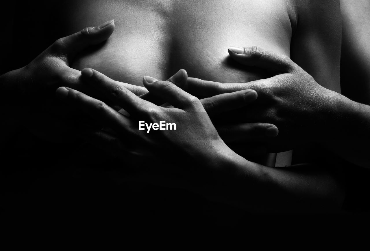 Cropped hands of woman covering shirtless girlfriend breasts