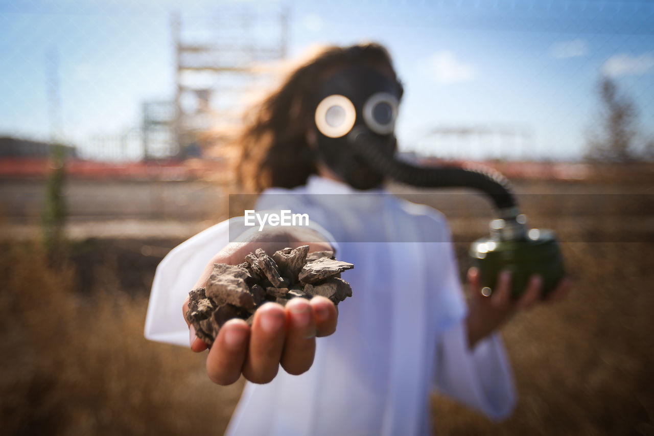 Girl wearing gas mask while holding stones on field