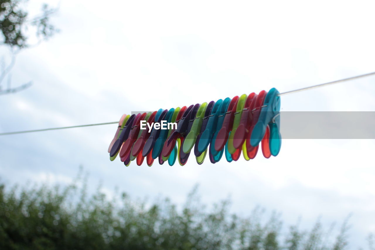 Low angle view of multi colored clothespins hanging against sky
