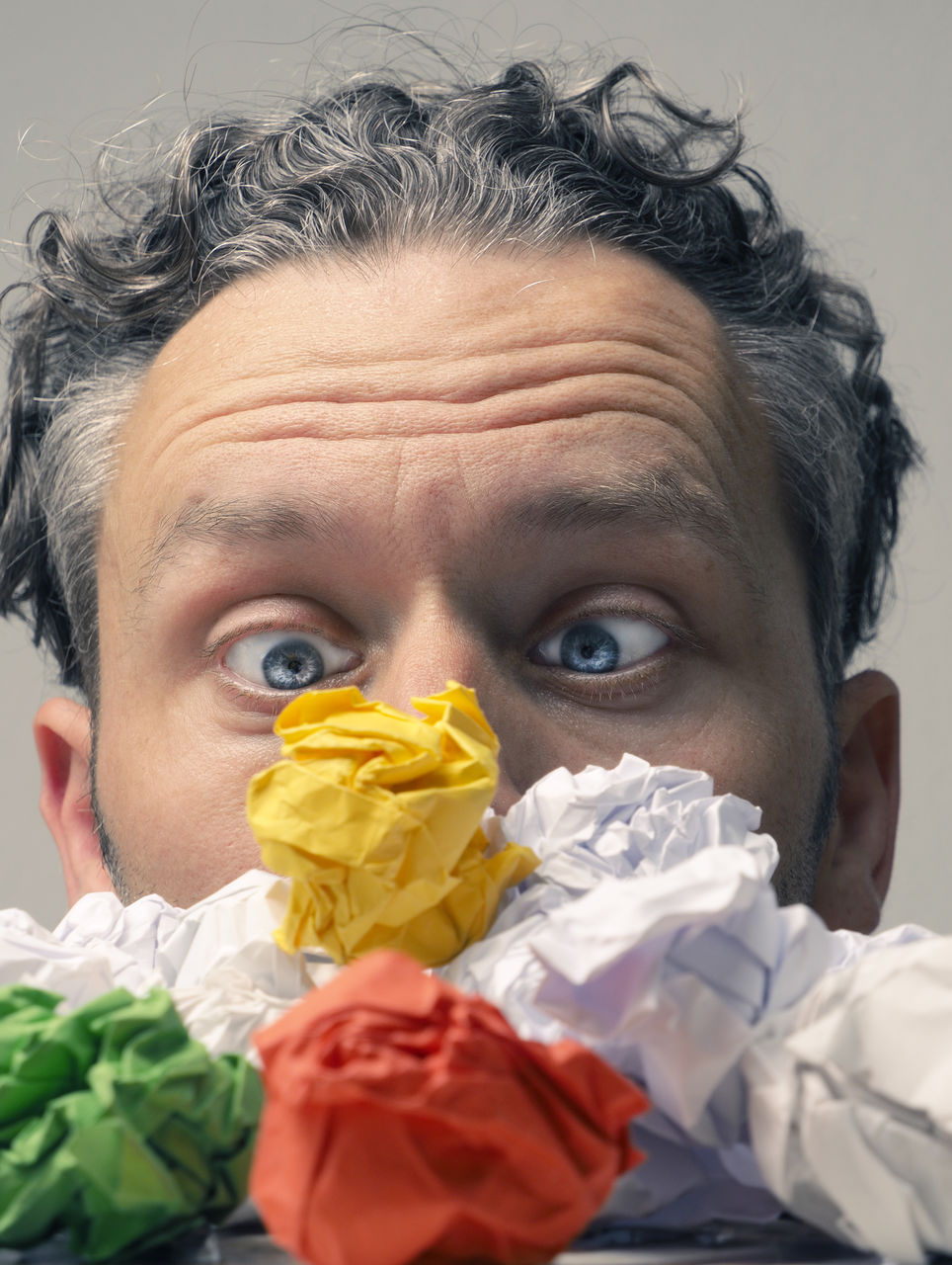 Close-up of surprised man looking at colorful crumpled papers