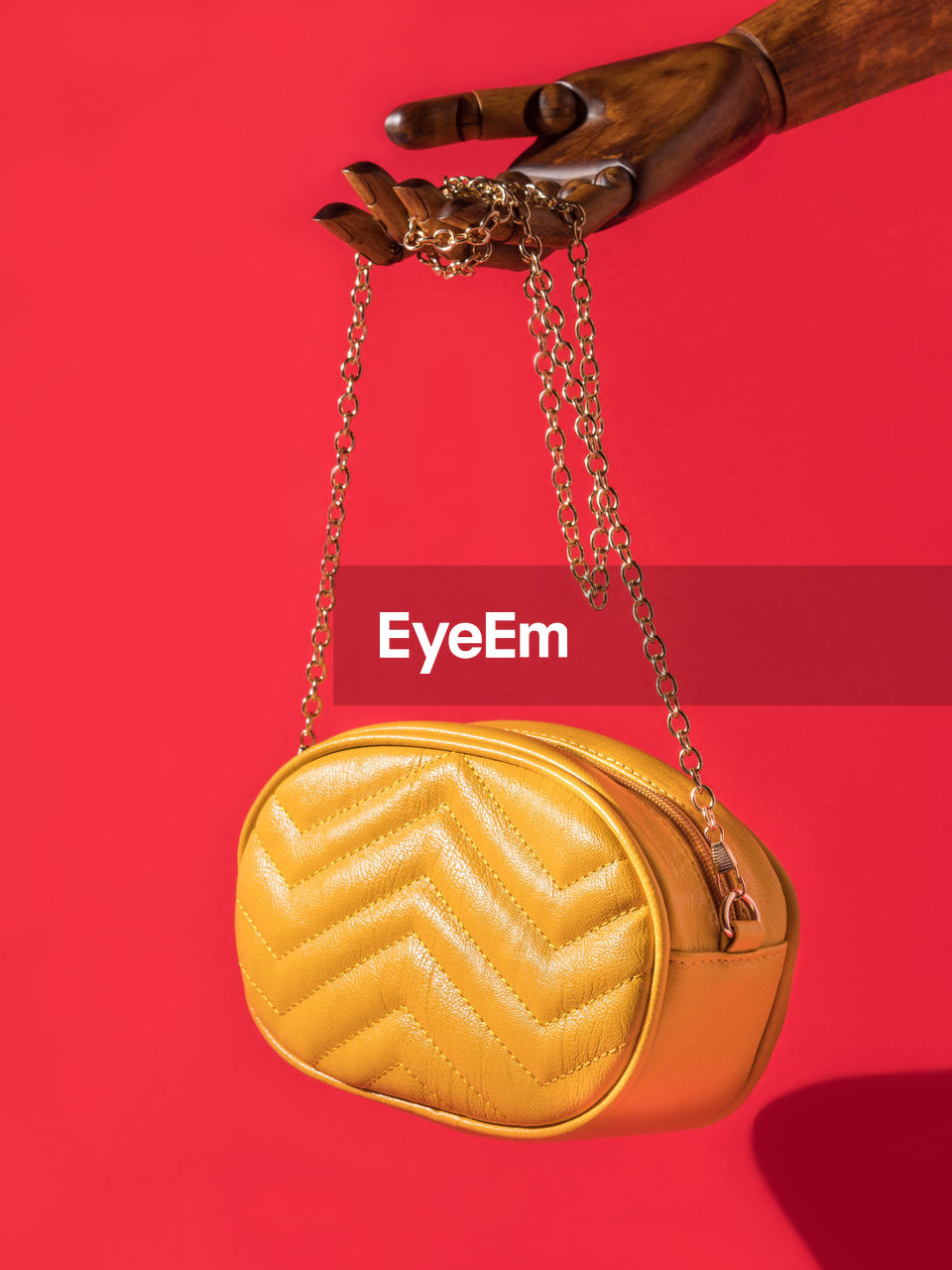 Wooden hand holding yellow eco leather bag on red background. female fashion accessories