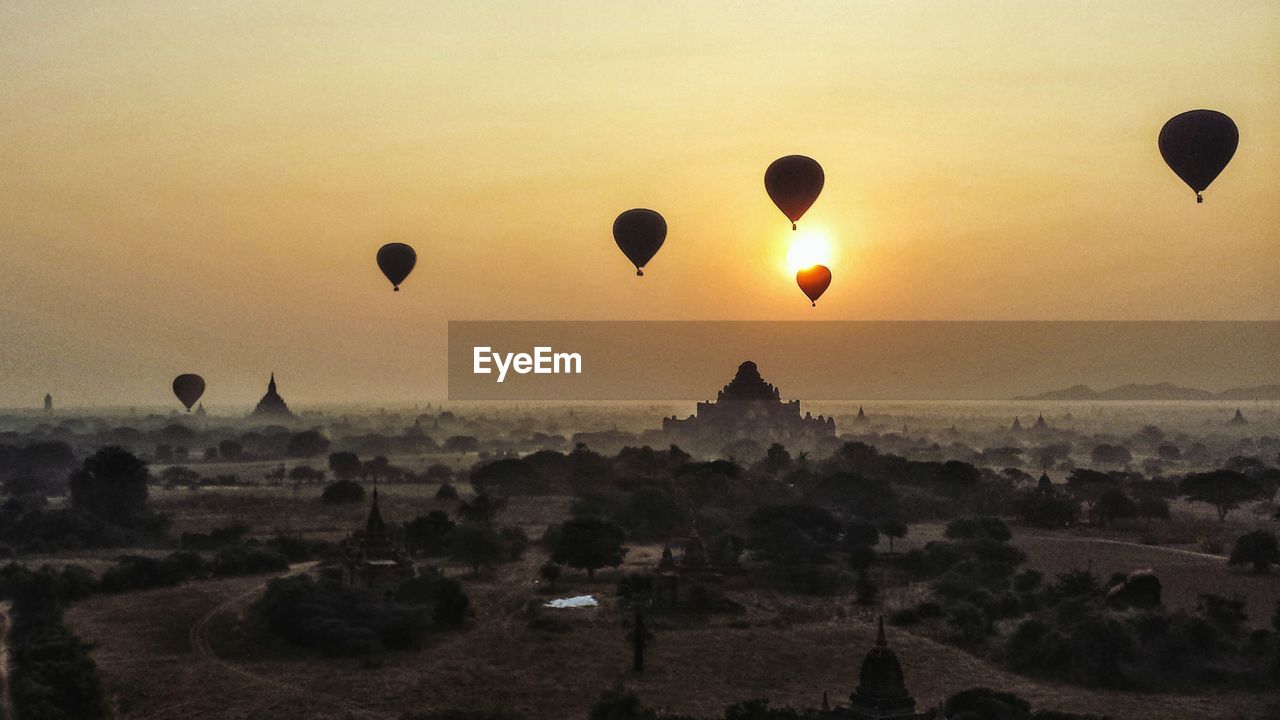 Silhouettes of hot air balloons flying over pagoda