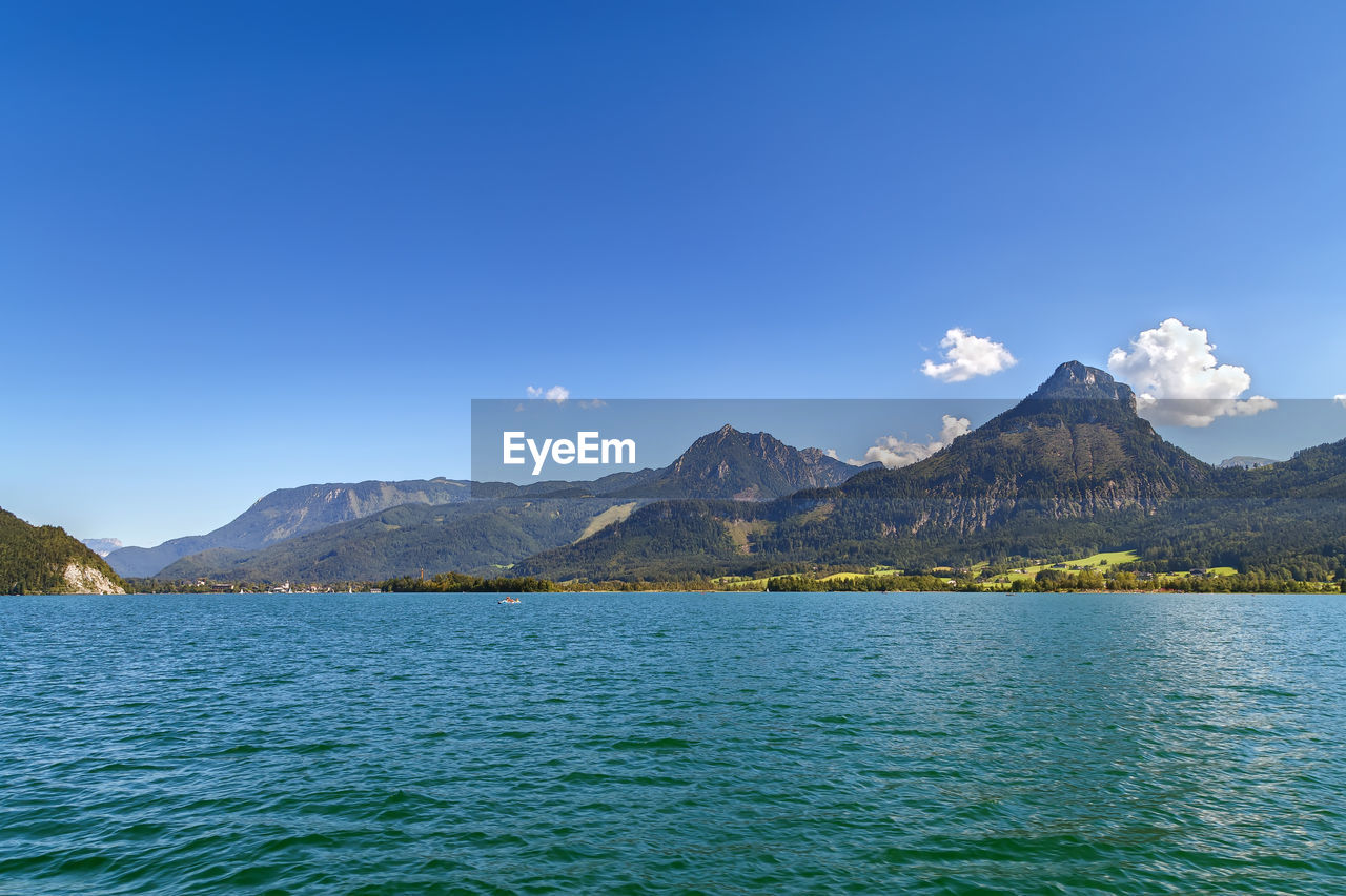 Scenic view of sea by mountains against blue sky