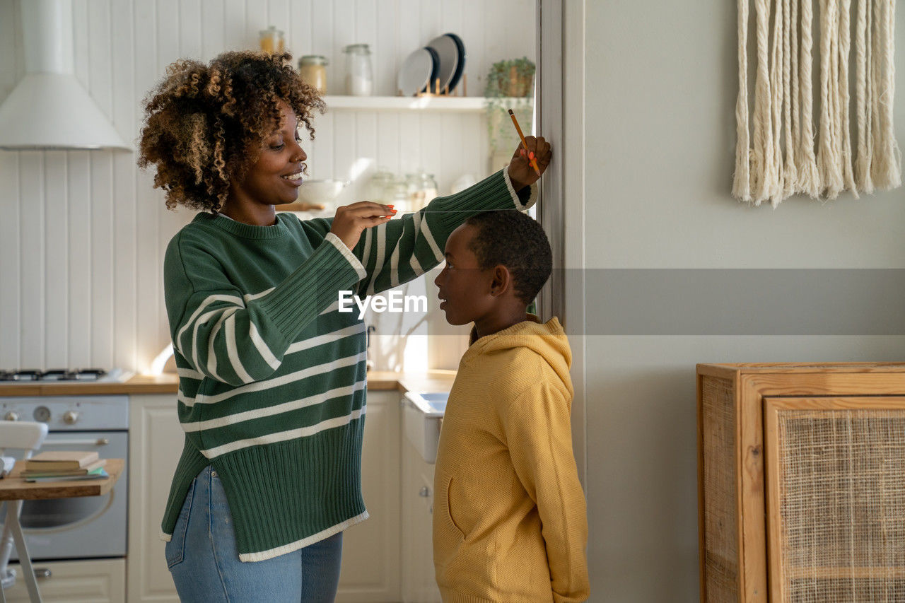 African american stay-at-home mom measuring height of kid son at home