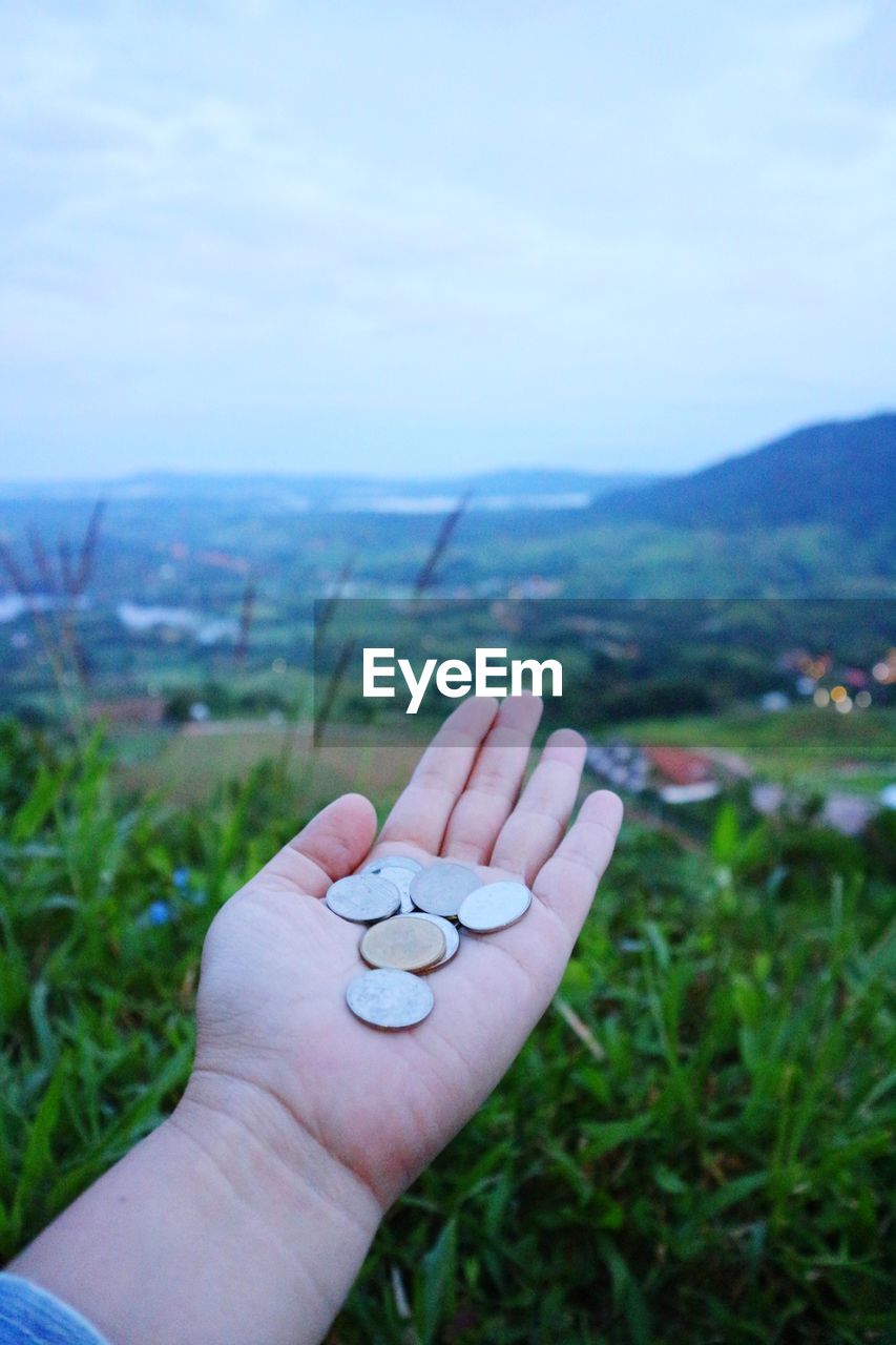 Cropped hand of woman holding coins against landscape