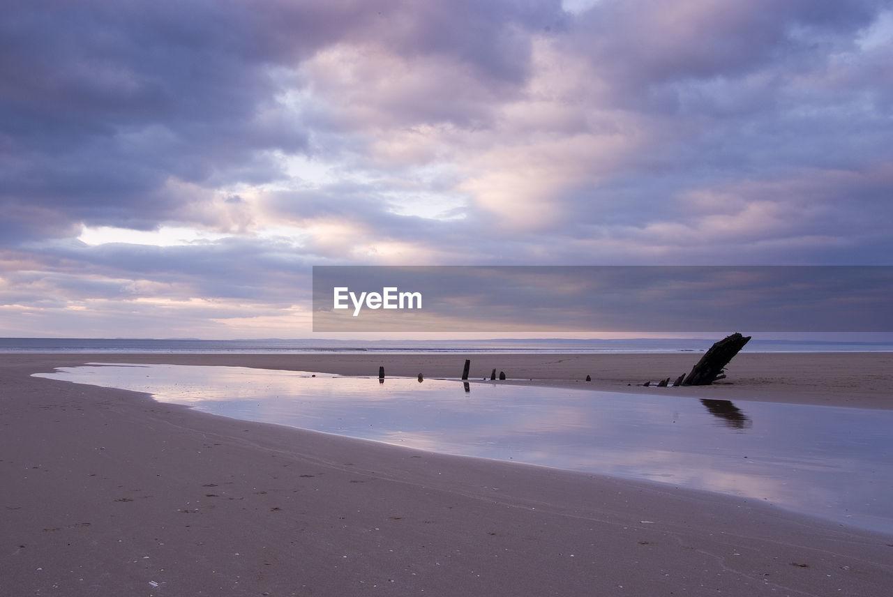 Scenic view of beach against cloudy sky at sunset