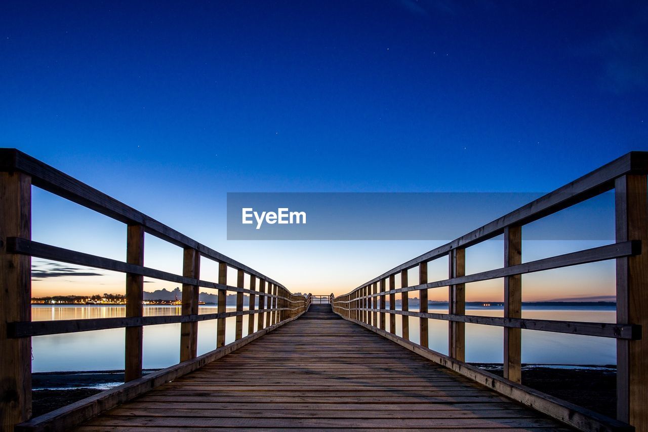 Footbridge over sea against clear sky during sunset