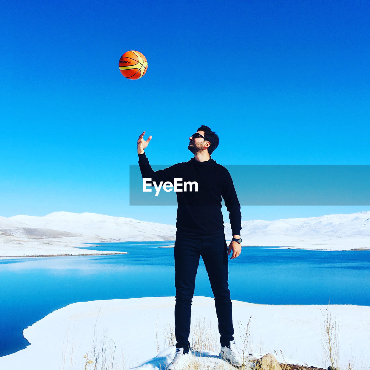 Full length of young man playing with basketball against lake during winter