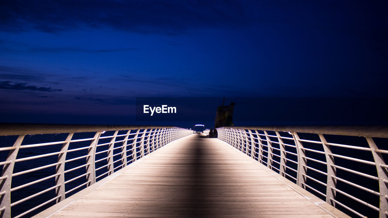 Jetty leading towards sea against sky at night