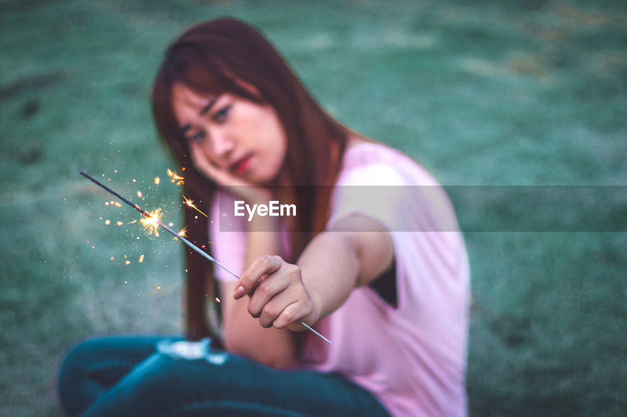 Portrait of woman holding sparkler while sitting on grass