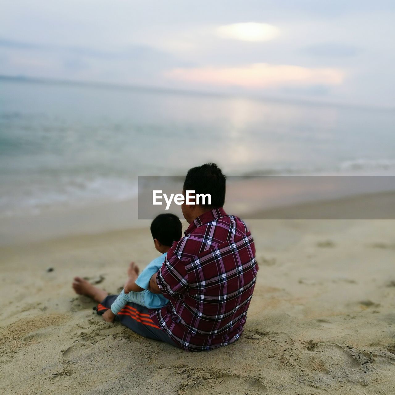 REAR VIEW OF WOMAN SITTING ON BEACH