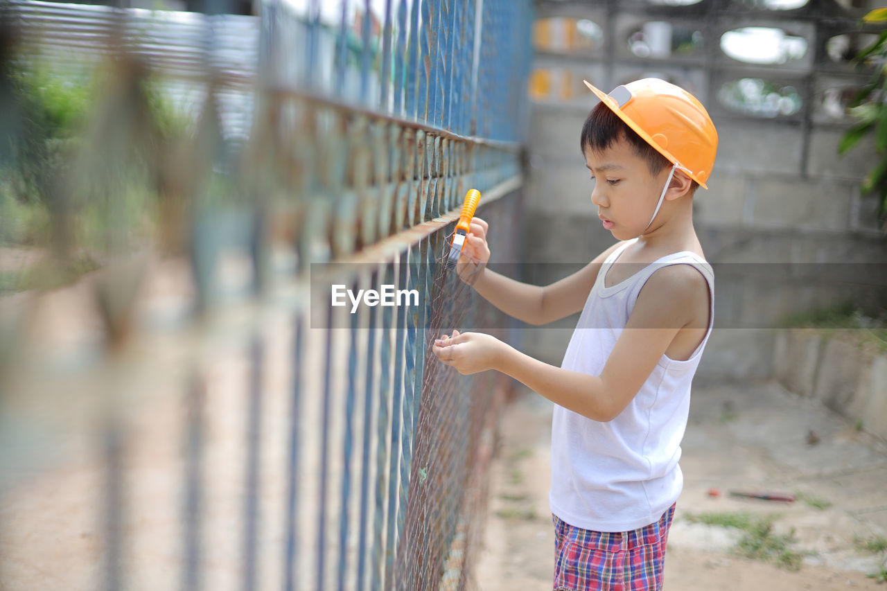 Side view of boy looking through fence